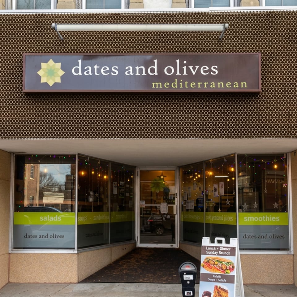 Dates and Olives Mediterranean restaurant storefront with honeycomb facade, illuminated windows, and sidewalk sandwich board.