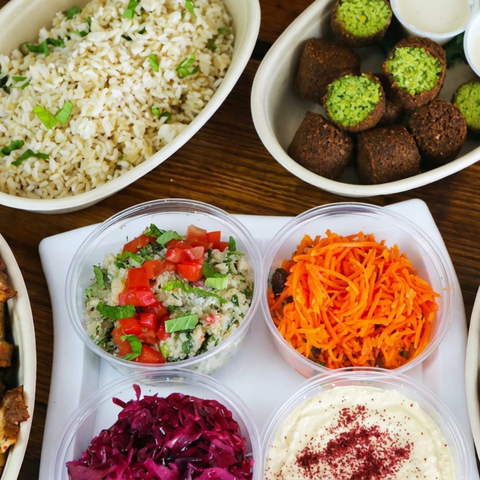 Middle Eastern feast with herbed rice, falafel, grilled chicken, pita bread, hummus, tabbouleh, carrots, and purple cabbage.